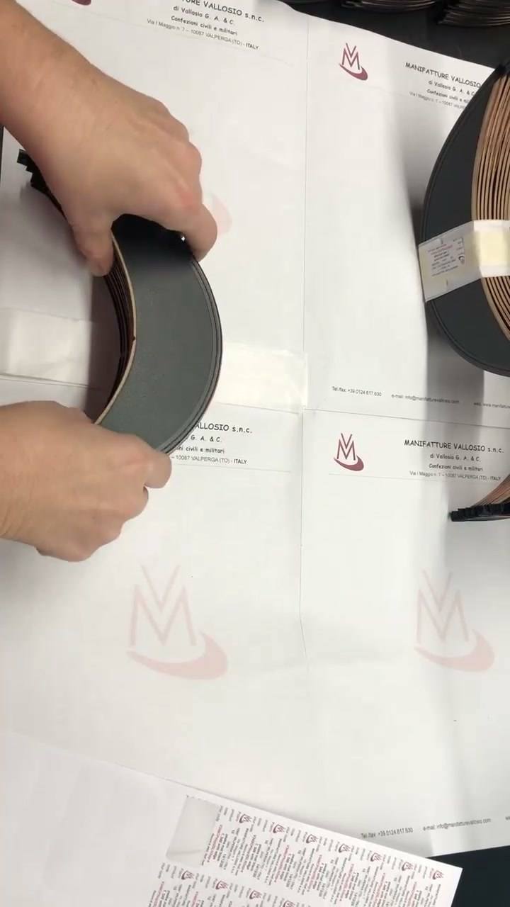 Mani che curvano una visiera nera sul banco, accanto a un rotolo di nastro
